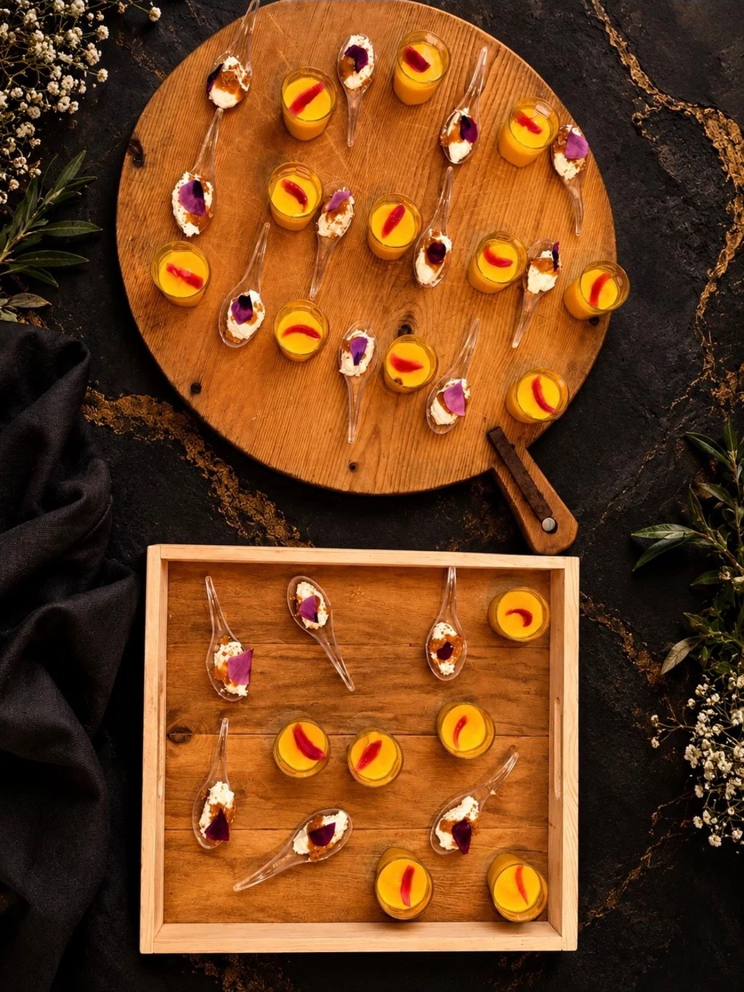 Amuse-bouches en cuillères garnies de pétales et verrines orangées, sur une planche et un plateau en bois